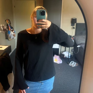 Svart blus med vida ärmar - Säljer en svart blus med långa, vida trumpetärmar och rund halsringning. Blusen har en rak passform och är tillverkad i ett mjukt tyg som känns skönt mot huden. Perfekt för dig som gillar stilrena plagg med en twist.