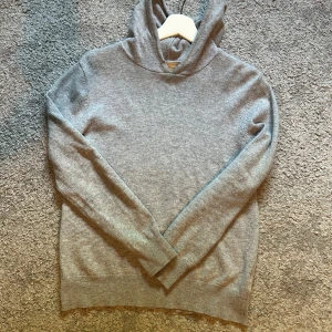 Grå kashmirhoodie från Sayless - Supermjuk och stilren grå hoodie i kashmir från Sayliss. Tröjan har lång ärm, huva och ribbade muddar. Perfekt för dig som gillar en clean look med lyxig känsla. Passar till allt och är riktigt skön att ha på sig.