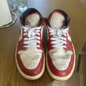 Nike Air Jordan 1 Low Chicago - Säljer ett par Nike Air Jordan 1 Low i klassiska Chicago-färger. Skorna har röd och vit ovandel i skinn med svarta detaljer och vita snören. Ikonisk Jordan-logga på hälen och tungan. Perfekta för dig som gillar streetwear och sneakers med retrovibe. En lila fläck på som ni kan se.