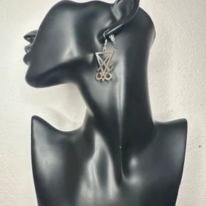 Handgjorda & unika örhängen med Lucifers Seal Wicca Witchy Ockult Metal Goth  - Handgjorda örhängen från Bybasen med Lucifers sigill som motiv – kraftfull symbol inom alternativ estetik. Ca 5 cm långa med stämplade, nickelsäkra krokar i äkta silver. Nya och aldrig använda. Perfekta för dig som gillar ockulta eller grafiska detaljer i din stil. Ingen prutning, men jag erbjuder rabatt vid köp av flera saker. Jag rensar garderob och smyckesskrin – kika gärna på mina andra annonser också!  