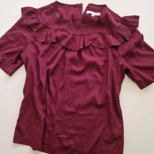 Vinröd blus med volangdetalj - Supersöt vinröd blus med korta ärmar och volang er.