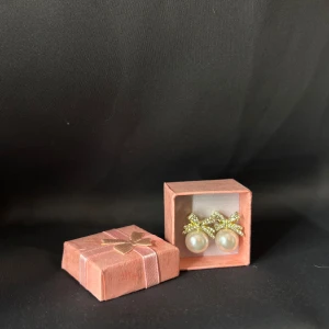 Guldiga örhängen med pärlor och rosett - Supersöta örhängen med gnistrande guldiga rosetter och stora vita pärlor. Rosetterna är täckta av små glittrande stenar som ger extra bling. Perfekta för dig som vill ha något gulligt och elegant på samma gång. Kommer i en söt rosa presentask med rosett. Helt oanvända då guld inte är min färg. Vet inte vart den kommer ifrån därav priset! 