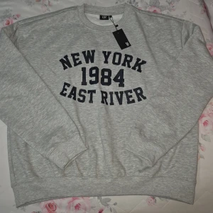 Grå sweatshirt med tryck från 157 - Snygg grå sweatshirt från 157 med svart tryck 'New York 1984 East River' på bröstet. Klassisk rund halsringning och långa ärmar. Perfekt för en avslappnad streetstyle-look.