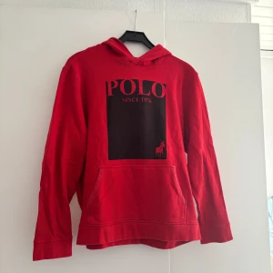 Röd hoodie från Polo Ralph Lauren - Röd hoodie från Polo Ralph Lauren med stor svart logga och texten 'POLO SINCE 1976' på bröstet.   Passar mest S men också M
