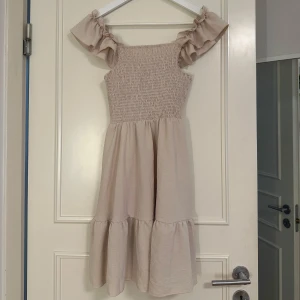 ljusbeige klänning - Supersöt ljusbeige kortklänning med volangiga axelband. Klänningen har en luftig kjol med mycket stretch. Materialet känns mjukt och lätt, och modellen är ärmlös med fina gulliga detaljer, säljer pågrund av att den inte passar längre och har blivit använd.