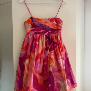 Färgglad kort sommarklänning med mönster - Superfin kort klänning med tunna axelband och färgstarkt blommigt mönster i rosa, orange och lila toner. Väldigt populär och är slutsåld på hemsidan