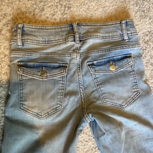 Ljusblå jeans bootcut med dubbla knappar - Snygga ljusblå jeans. Byxorna har dubbla knappar i midjan, klassiska fickor fram och bak med lock och knappdetaljer. 