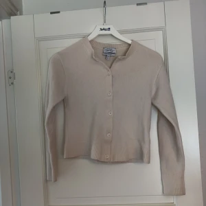 Beige kofta i merino ull från & Other Stories - Supermjuk beige kofta från & Other Storie i 100% merinoull. Klassisk rak modell med rund halsringning, ribbade muddar och knäppning framtill med sex knappar. Passar mer som XXS än XS