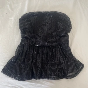 Svart glittrig bandeau tubtopp - Supersnygg svart bandeau tubtopp med glittriga paljetter över hela toppen. Volang nertill ger en extra cool touch och toppen är perfekt för utekvällar! Säljer för att få plats i garderoben🩷      #stockholmstyle 