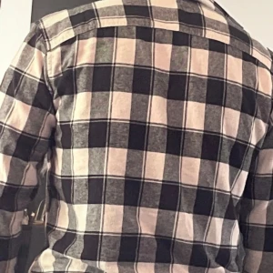 Rutig beige och svart skjorta storlek M - Säljer en snygg rutig skjorta i beige, svart och grå toner. Skjortan har långa ärmar och klassisk krage, med knappar framtill. Perfekt att bära öppen över en t-shirt för en chill look. Materialet känns mjukt och bekvämt mot huden.