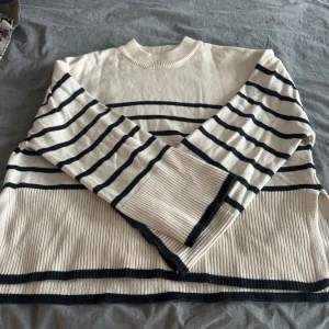 Randig beige och svart stickad tröja - Snygg stickad tröja i beige med svarta ränder. Tröjan har rund halsringning, långa ärmar och ribbade muddar samt nederkant. Perfekt för dig som gillar en klassisk och stilren look med en twist.