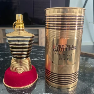 Jean Paul Gaultier Le Male Elixir 125ml - Säljer en lyxig parfym, Le Male Elixir från Jean Paul Gaultier. Flaskan är formad som en manlig torso i guld och mörkrött glas med metalliska ränder. Kommer i en snygg guldfärgad burk. Volymen är 125 ml. Perfekt för dig som gillar exklusiva dofter och cool design.