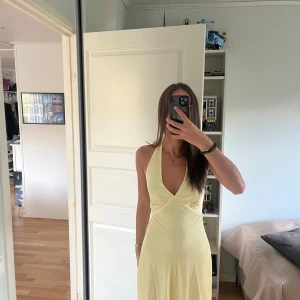 Ljusgul långklänning med knyt i ryggen - Supersnygg ljusgul långklänning med djup v-ringning och knyt i nacken och ryggen. Klänningen har en öppen rygg och är i satinliknade material. Prislapp kvar! Går att pruta