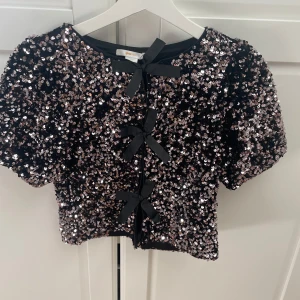 Svart paljettopp med rosetter Gina Tricot - Glittrig svart topp från Gina Tricot, med små rosetter. Storlek 146/152💞
