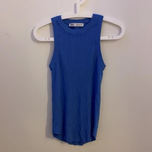 Blå ribbad linnetopp från Zara - Snygg blå ribbad linnetopp från Zara med rund halsringning och ärmlös design. Toppen har en rak passform och är tillverkad i ett stretchigt material som sitter skönt på kroppen. Perfekt att styla med jeans eller kjol för en fräsch look. Pris kan diskuteras!