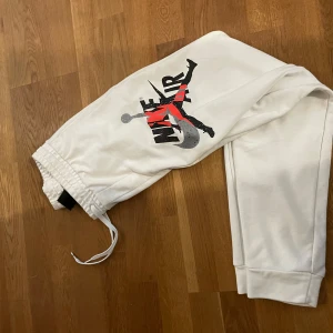 Vita Jordan mjukisbyxor med tryck - Snygga vita mjukisbyxor från Jordan med stort Nike Air-tryck och Jumpman-logga på benet. Byxorna har resår och snörning i midjan samt muddar vid bensluten. Perfekta för en sportig och avslappnad stil.