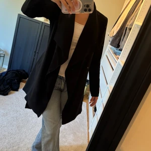 Svart omlottkappa med bälte - Snygg svart kappa i omlottmodell med bälte i midjan och långa ärmar. 