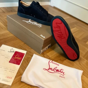 Mörkblå sneakers från Christian Louboutin - Snygga mörkblå sneakers från Christian Louboutin med ikonisk röd sula och diskret broderad logga på hälen. Skorna är tillverkade i mjuk mocka och har rund tå, snörning och platt sula. Perfekt för dig som vill sticka ut med exklusiv stil och detaljer. Det är storlek 40 men dom är ganska små i storleken 