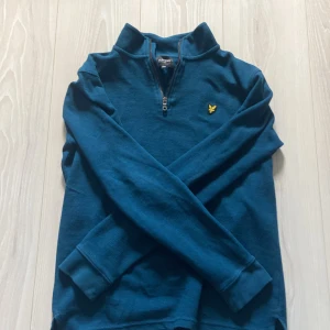 Blå half zip tröja från Lyle & Scott - Snygg blå långärmad tröja från Lyle & Scott med half zip och klassisk gul logga på bröstet. Tröjan har ribbade muddar och är gjord i mjuk bomull, perfekt för en chill och stilren look. Priset är ej hugget i sten.