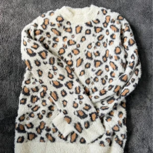 Leopardmönstrad fluffig tröja - Supermjuk och fluffig tröja med leopardmönster i beige, svart och brunt. Rund halsringning och långa ärmar. Perfekt för dig som vill sticka ut och hålla dig varm under kyliga dagar.