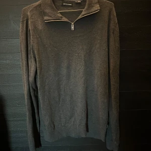 Mörkgrå half zip (Jack & Jones) - Mörkgrå långärmad tröja från Jack & Jones med stilren half zip-dragkedja vid kragen. Tröjan har en klassisk passform och är perfekt till hösten. 
