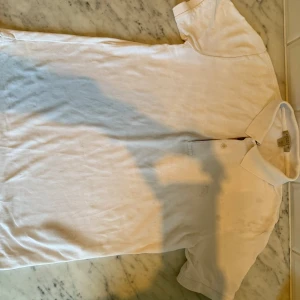Vit pikétröja från Burberry Brit XS - Vit pikétröja från Burberry Brit i klassisk modell med krage och två knappar framtill. Tröjan har diskret broderad logga på bröstet och är tillverkad i mjuk bomull. Perfekt för en clean och stilren look.