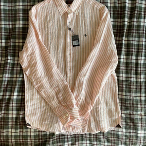 Randig linneskjorta från Morris L - Snygg randig skjorta från Morris i ljus orange och vitt. Tillverkad i svalt linne, perfekt för varmare dagar. Klassisk krage, knäppning framtill och broderad logga på bröstet. Långärmad och med en avslappnad passform. Inköpt för 1400 aldrig använd så riktigt kap behöver ba cash så vill få iväg den asap 👍 skriv om ni vill ha fler bilder eller annat ni funderar över 
