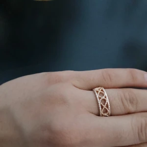 Bred guldfärgad ring med pärldetaljer - Snygg bred ring i guldfärg roseguld med ett öppet, flätat mönster och små pärldetaljer längs kanterna. Ringen har en elegant och unik design som verkligen sticker ut. Perfekt accessoar för att lyfta din stil.