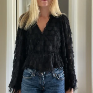 Svart blus med fransiga detaljer - Säljer en svart blus med v-ringning och lång ärm. Blusen har ett unikt fransigt mönster 