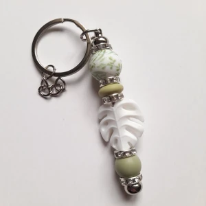 Nyckelring med pärlor och blad - Handgjord nyckelring med silverfärgad ring, dekorerad med gröna och vita silikonpärlor samt glittriga mellandelar. Perfekt att hänga på väskan eller nycklarna för en personlig touch.