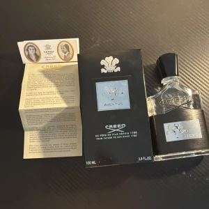 Creed Aventus Eau de Parfum 100ml - Lyxig parfym från Creed, Aventus, i en elegant genomskinlig glasflaska med svart och silverdetaljer. Flaskan rymmer 100 ml och har en svart kork. Kommer med originalkartong och informationsblad. Doften är ikonisk och exklusiv, perfekt för dig som gillar klass och stil. Pris kan sänkas vid snabb affär. 