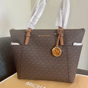 *NY*Jet Set Item Väska Fr Michael Kors - Säljer en ny Michael Kors Jet Set Item EW TZ Tote väska i färgen BRN/Acorn. Mörkbrun, snygg till hösten. Ny med lappar inkl dustbag och MK kasse om så önskas. Nypris: 2800 kr, Outlet: 1859 kr, Mitt pris: 1200 kr. Product Description Introducing the Jet Set Item Ew Tz Tote, a must-have accessory for ladies who appreciate both style and functionality. This shoulder bag, brought to you by Michael Kors, is designed to elevate your fashion game to new heights. In a stunning brown acorn shade. 