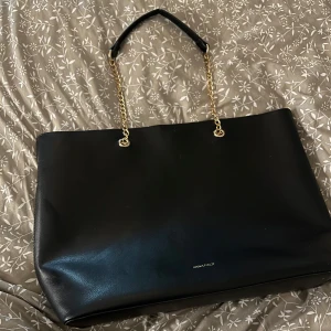 Svart axelväska från Anna Field - Stilren svart axelväska från Anna Field med guldfärgade kedjehandtag och detaljer. Väskan är tillverkad i skinnimitation och har magnetlås upptill. Perfekt storlek för att få plats med allt du behöver och snygg att bära över axeln.