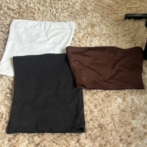 3-pack bandeau tubtoppar i basfärger - Tre bandeau tubtoppar i svart, vitt och brunt. Alla har en tight passform. Gjorda i mjukt och stretchigt material som sitter skönt mot kroppen. Svart och vit från bikbok och bruna från nly trend