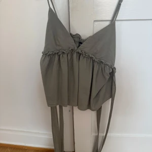 Grå omlottopp med knyt från Zara - Supersöt grön topp från Zara med smala axelband och volangdetaljer. Toppen har knytband i midjan.