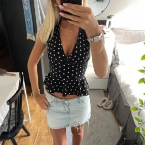 Svart prickig halterneck topp - Snygg svart halterneck topp med vita prickar och djup v-ringning. Toppen har figurnära passform och volangkant nertill. Tryck på KÖP NU så postar jag så snabbt som möjligt!! 🩷
