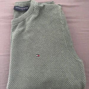 Grön stickad tröja Tommy Hilfiger L - Snygg grön stickad tröja från Tommy Hilfiger i storlek L. Tröjan har ett diskret mönster, rund halsringning och klassisk logga broderad på bröstet. Tillverkad i 100% bomull för en skön och avslappnad känsla.