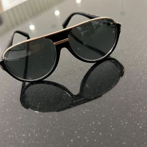 Svarta aviator-solglasögon - Snygga svarta aviator-solglasögon  med tunna guldfärgade detaljer längs ovankanten och runt bågarna. Glasen är mörka och ramen har en klassisk, stilren design som ger en cool vibe. Perfekta för att lyfta din look i sommar.