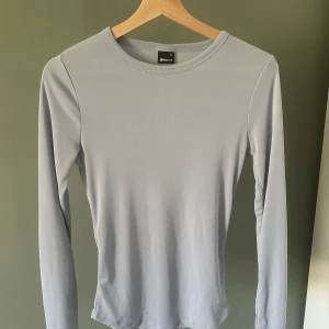 Ljusgrå långärmad tröja Gina Tricot - En stilren ljusblå långärmad tröja från Gina Tricot. Tröjan har en rund halsringning och är tillverkad i mjuk bomullsmix som sitter skönt mot kroppen. Perfekt att matcha med jeans eller kjol för en clean look.