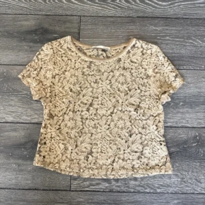 Beige spetsblus från Oui - Superfin beige blus från Oui i spets med blommigt mönster. Kortärmad och med rund halsringning. Sidenliknande kant vid halsen ger en extra lyxig känsla.