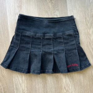 Svart plisserad jeanskjol från BDG - Snygg svart kort jeanskjol från BDG Jeans med plisserad design och broderad logga i rött. Kjolen har dragkedja i sidan och en bred linning som ger en cool siluett. 