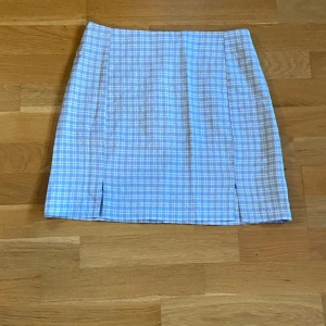 Blåvit rutig kortkjol! Nyskick!  - Supersöt blå och vit rutig kortkjol.Kjolen har en rak passform, liten slits framtill och dragkedja i sidan. Perfekt för dig som gillar preppy vibes och vill ha en fräsch look till våren eller sommaren. Ljusblå vit Dragkedja bak  2 slitsar fram 8 cm Längd 40 cm   Perfekt nyskick  Färgen är som på de 2 sista bilderna  