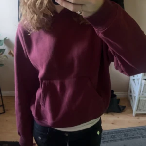 Vinröd hoodie med huva - Säljer en vinröd hoodie med huva och stor magficka. Tröjan har en relaxed passform och är perfekt för chill dagar. Mjuk bomullskänsla och långa ärmar. Enkel och stilren design utan tryck eller mönster.