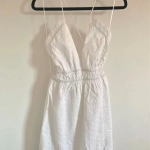 Vit långklänning med snörning från Zara - Superfin vit långklänning från Zara med broderade detaljer och smala axelband. Djup v-ringning, snörning i ryggen och slits framtill. Perfekt för sommarens varma dagar, i luftig bomull med romantisk känsla.