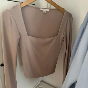 Beige långärmad topp från Amisu - Säljer en stilren beige topp från Amisu med lång ärm och fyrkantig urringning. Toppen är figurnära och har en clean look utan mönster eller detaljer. Perfekt att matcha med jeans eller kjol för en enkel men snygg outfit. 