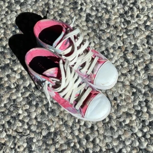 Heelys x Tommy Hilfiger sneakers rosa - Färgglada Heelys sneakers i samarbete med Tommy Hilfiger, med coolt batikmönster i rosa, vitt och ljusblått. Skorna har vita snören, rund tå och vit tåhätta. Utrustade med hjul i sulan för att rulla fram. Perfekta för dig som vill sticka ut.