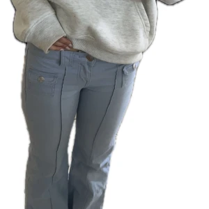 Ljusblå/lila  bootcut byxor med fickor - Populära ljusblå/lila jeans från  hm som har bootcut passform och dekorativa fickor framtill med lock och knapp. Byxorna har låg midja och markerade sömmar längs benen. Perfekta för en trendig och avslappnad look.