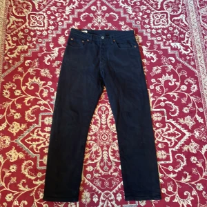 Svarta Levi's 501 jeans - Säljer ett par svarta Levi's 501 jeans med klassisk rak passform. Jeansen har fem fickor, knappgylf och den ikoniska läderpatchen bak i midjan. Materialet är robust denim och färgen är djup svart, perfekt till en clean och tidlös look.