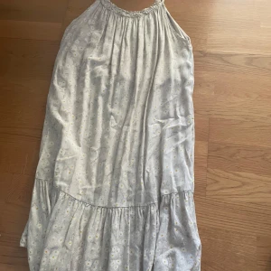 blommig långklänning - Supersöt långklänning med små vita och gula blommor. Klänningen har volang. Perfekt för varma dagar när du vill känna dig extra somrig och chill.