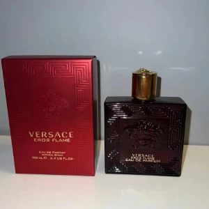 Versace Eros Flame Eau de Parfum - Versace Eros Flame Eau de Parfum 100 ml med lyxig röd glasflaska och guldfärgat lock. Flaskan har en elegant Medusa-detalj och geometriskt mönster. Kommer med matchande röd kartong med guldtext. Doften är intensiv och modern.